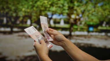 Şehir parkında İzlanda Krona banknotları tutan adam, doğal güneş ışığı altında para yatırımı ve ticari işlemleri sembolize ediyor..