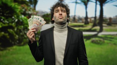 Parkta Arjantin pezosu tutan adam resmi giyinmiş, yeşil ve palmiye ağaçlarıyla çevrili, kendine güvenen bir ifadeyle zenginlik sergiliyor..