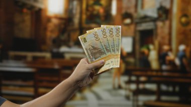 Bir kilisede Norveçli kronlar tutan bir adam. İçerideki aydınlatma ve el hareketleriyle finans ve inancın yan yana gelişini yakalıyor..