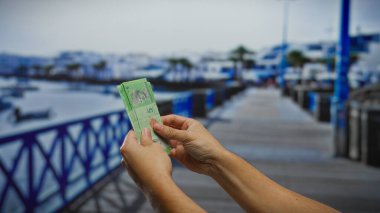 Man holding malaysian ringgits on a seaside street with blurred background of a port and boats. clipart