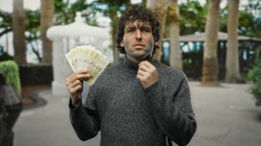 Norveç Kronu 'nu elinde tutan adam, şehir sokaklarında, palmiye ağaçları ve kentsel arka planda tefekküre daldığını ifade ediyor..