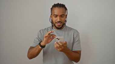 Örgülü genç adam beyaz arka planda akıllı telefon kullanıyor, modern teknolojiye odaklanmış sıradan bir stil sergiliyor ve izole edilmiş bir yetişkin ortamı var..