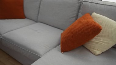 Oturma odasının iç kısmında, dokulu turuncu ve beyaz yastıklarla süslenmiş rahat gri bir kanepe var. Modern ve davetkar bir ev atmosferi yaratıyor..