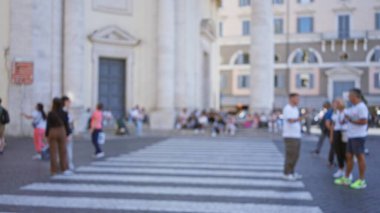 Bulanık insanlar Roma, İtalya 'daki Piazza del Popolo' da karşıdan karşıya geçiyor. Arka planda tarihi mimari ve hareketli sokak hayatı var. Canlı bir şehir manzarası yaratıyor..