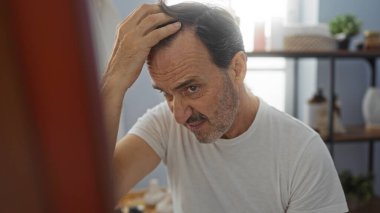 Sağlık merkezindeki saçı inceleyen olgun İspanyol bir adam güzellik salonunun iç kısımlarında güzellik ürünleriyle sakin bir sahne yaratıyor..