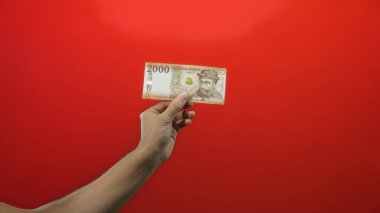 Macar forint banknotunu elinde tutan adam kırmızı arkaplan karşısında çarpıcı bir kontrast yaratıyor ve para birimi özelliklerini vurguluyor..