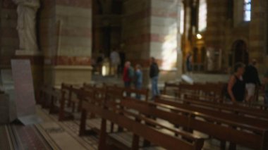 Ahşap sıraları ve heykelleri olan bir kilisenin içindeki insanların bulanık görüntüsü. Tarihi bir Hıristiyan ortamında dinsel bir atmosfer yakalıyorlar..