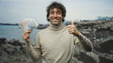 Sahilde gülümseyen İspanyol adam zloti banknotları tutuyor, kumsalın arka planında onayını veriyor..