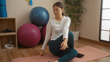 Spor salonunda yoga yapan, arka planda egzersiz topları olan bir kadın spor salonunda spor yapmak ve içeride dikkat çekmek için sakin bir Asyalı ortamı sergiliyor..