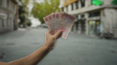 Bir şehir caddesinde elinde lira banknotları tutan Türk bir adam, açık şehir ortamında finans kavramını sergiliyor.