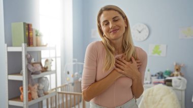 Yumuşak oyuncaklar ve bebek beşiği ile çevrili, sıcak ve sevgi ifade eden, samimi yatak odasında elleri üzerinde gülümseyen bir kadın..