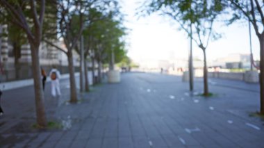 Marsilya sokaklarında ağaçlar ve dağılmış binalarla yürüyen bir kadının bulanık görüntüsü huzurlu bir şehir atmosferini yükselten bir bokeh arka plan yaratıyor..