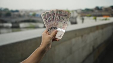 Man holding saudi arabian riyal banknotes in hand outdoors on a city street offering a cultural glimpse of currency exchange and economy in saudi arabia during daytime.