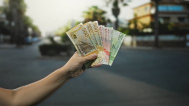 Norveç kronu banknotları elinde tutan bir adam bir şehir sokağında duruyor, açık bir şehir ortamında nakit para gösteriyor, bulanık bir geçmişi var, ekonomik aktiviteyi vurguluyor..