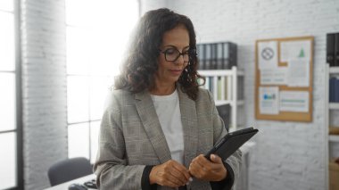 Modern ofis ortamında tablet kullanan bir kadın, parlak iç tasarım unsurlarının yer aldığı bir iş ortamında teknolojiyle olgunlaşmış profesyonel etkileşim sergiliyor..