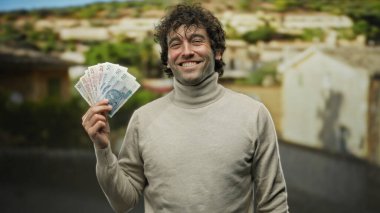 Sokak ortasında gülümseyen İspanyol bir adam elinde Polonya zloti banknotları ile para ve başarı sergiliyor..