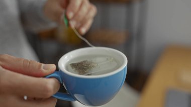 Ofisteki genç adam mavi bardakla çay demliyor ve ellerini iş yerinde gösteriyor..