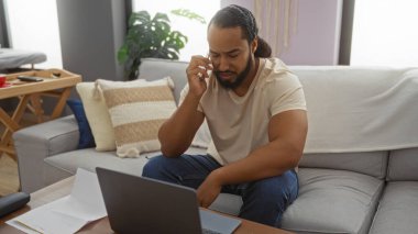 Oturma odasındaki koltukta oturan genç adam uzaktan iletişim için günlük bir ev ayarını işaret ediyor.