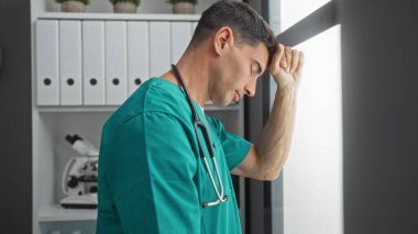 Klinik dinlenme odasında önlük giymiş, mikroskop takmış, iş yerinde stres olduğunu iddia eden düşünceli bir adam.
