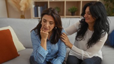 İki orta yaşlı kadın rahat bir oturma odasındaki kanepede rahat bir anı paylaşıyor. Aile desteği ve dostluğun vücut bulmuş hali..