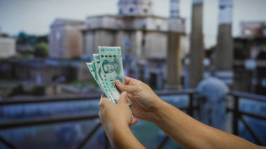 Roma forumunda antik mimarinin önünde Çin yuanı banknotları tutan adam açık havada küresel finansmanı vurguluyor..