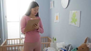 Sıcak bir yatak odasında beşiği olan, renkli çizimler ve yumuşak oyuncaklarla çevrili bir kadın. Huzurlu bir ev ortamı yaratıyor..