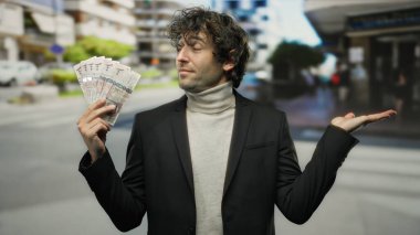 Bir şehir caddesinde İspanyol bir adam Suudi riyal banknotlarını geniş bir el ile tutuyor, kentsel bir arka planda zenginlik veya güven taşıyor..