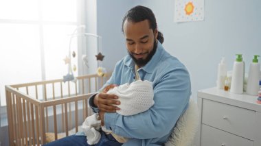 Sakallı genç adam rahat bir yatak odasında bebek beşiği yapıyor. Ev ortamında sıcaklık ve rahatlık yayıyor..