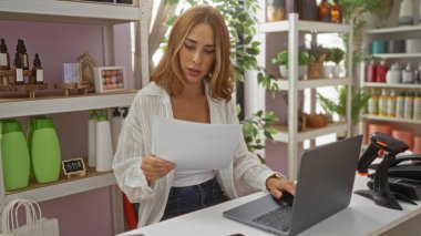 Dekoratif ev dekorasyonunda doküman okuyan genç bir kadın. Etrafı ürün ve bitkilerle çevrili.