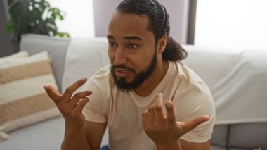 Samimi oturma odasında el kol hareketi yapan sakallı genç bir adam, kapalı alanda etkileyici bir iletişim kuruyor..