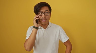 Sarı arka plan önünde cep telefonuyla konuşan genç Çinli bir adam ciddi ifadeyi sıradan tarzla harmanlıyor.