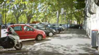 Roma 'daki bulanık sokak sahnesinde park halindeki arabaların ve ağaçların odak noktasında eski bir kasaba yoluna dizildiğini, açık İtalyan hayatının özünü yakaladığını gösteren bir bokeh etkisi var..