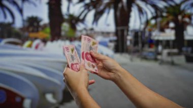 Kentsel caddede Meksika pezosu tutan adam palmiye ağaçlarının altında açık hava mali işlemleri veya yatırım kavramını gösteren arabalar taşıyor..