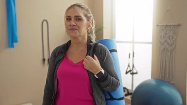 Beden eğitimi paspasındaki kadın, gülümsüyor ve el kol hareketleri yapıyor. Spor kıyafetleri giyiyor. Spor kıyafetleri giyiyor..