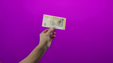 Danimarka ve ekonomi üzerine net bir odak noktası olan, finans ve para birimini sembolize eden, canlı mor bir arkaplan karşısında Danimarka kronu tutan bir el..