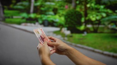 Yeşil şehir parkı ortamında Norveç kronu banknotları tutan adam, iş, yatırım ve açık hava finans kavramını vurguluyor.