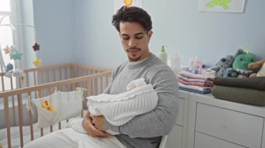 Genç bir adam yatak odasında beşiği ve içi doldurulmuş hayvanlarla evde huzurlu bir aile ortamını gösteriyor..