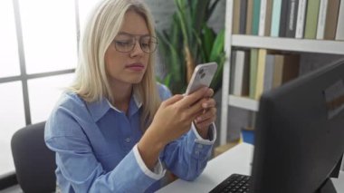 Modern ofis ortamında akıllı telefon kullanan bir kadın, kitap rafları ile bilgisayar masası gözlüğü profesyonel ifade işi, bitkileri iç mekanda sarışın yapıyor.