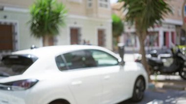 Güneşli bir günde arka planda palmiye ağaçları ve binalar olan açık bir sokakta bulanık beyaz bir araba.