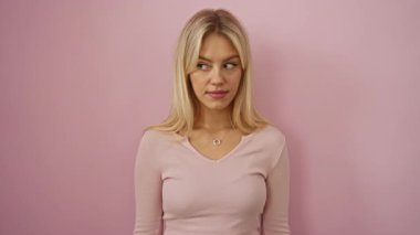 Pembe arka planda poz veren, sarı saçlı, rahat giyinen, doğal güzellik ve dingin ifade sergileyen, kadınsı cazibe ve modern zarafeti ön plana çıkaran bir kadın..