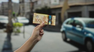 Şehir geçmişi bulanık ve hareket halindeki arabalarla dolu kalabalık bir caddede elinde 100 dolarlık Kanada banknotunu tutan bir adam..