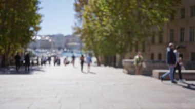 Ağaçlar ve binalar tarafından çerçevelenmiş, güneşli bir Marsilya caddesinde yürüyen bulanık insanlar Avrupa 'nın açık hava ortamında sakin bir atmosferik bokeh etkisi yaratıyor..