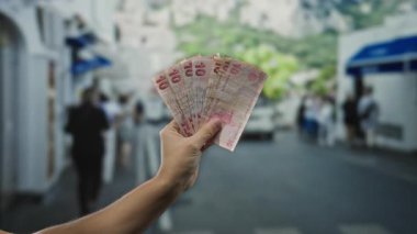 İşlek bir şehir sokağında el ele tutuşan Türk lirası banknotları. Arka planda insanlar var. Şehir hayatının ve ekonominin özünü yakalıyorlar..