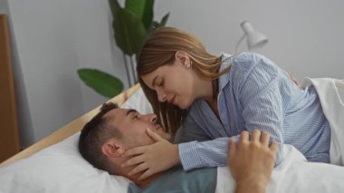 Yatak odasında kucaklaşan bir çift sevgi ve şefkat gösteriyor. Bir kadın, sıcak ve romantik bir atmosfer yaratarak, erkeği nazikçe kucaklıyor..