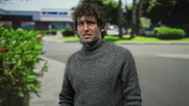 Şehirdeki genç adam arka planda yeşil bitkilerle sokakta el hareketi yapıyor, şehir ortamında yakışıklı bir erkek yakalıyor..