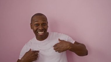 Genç adam gülümseyip pembe bir arka plana işaret ederek izole ve canlı bir ortamda mutluluk ve pozitiflik taşıyor..
