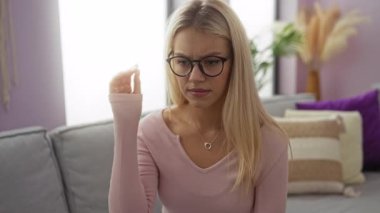 Gözlük çıkaran ve gözlerini ovuşturan bir kadın şık dekorlu ve yumuşak ışıklandırmalı rahat bir oturma odasında yorgun görünüyor. Bu da dinlenme ihtiyacı ya da ekran kullanımından kurtulma ihtiyacı olduğunu gösteriyor..