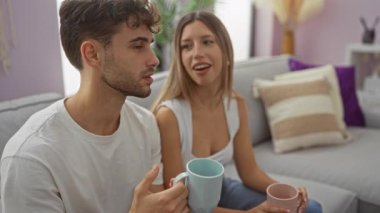 Bir çift, rahat bir oturma odasında rahatlıyor, kahvelerini yudumluyor ve rahat bir kanepede birlikte vakit geçiriyorlar..