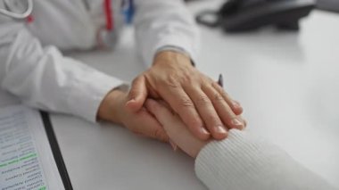 Hastane ofisinde hastanın elini tutan doktor güven bakımı empatisini ve profesyonel ilişkiyi vurguladı.