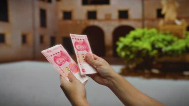 Bir şehir caddesinde Çin Yuan banknotları tutan bir adam, şehir geçmişi bulanık, açık havada iş ve para değişimi sergiliyor..